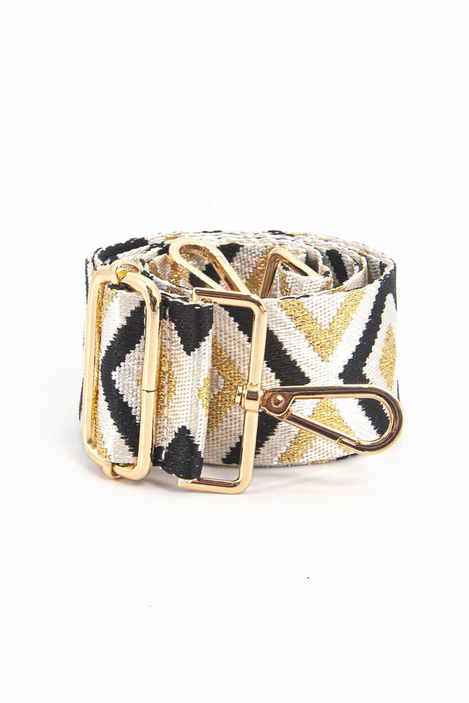 showing the bag strap coiled around itself, the gold and black metallic aztec pattern woven design is prominent , the gold hardware is shown in close up