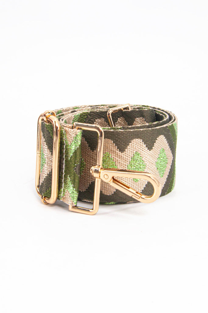 showing the bag strap coiled around itself, the green and gold metallic aztec pattern woven design is prominent , the gold hardware is shown in close up