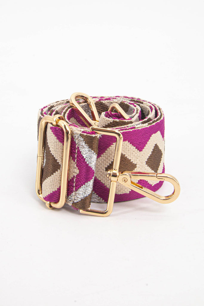 showing the bag strap coiled around itself, the pink and taupe aztec pattern woven design is prominent , the gold hardware is shown in close up