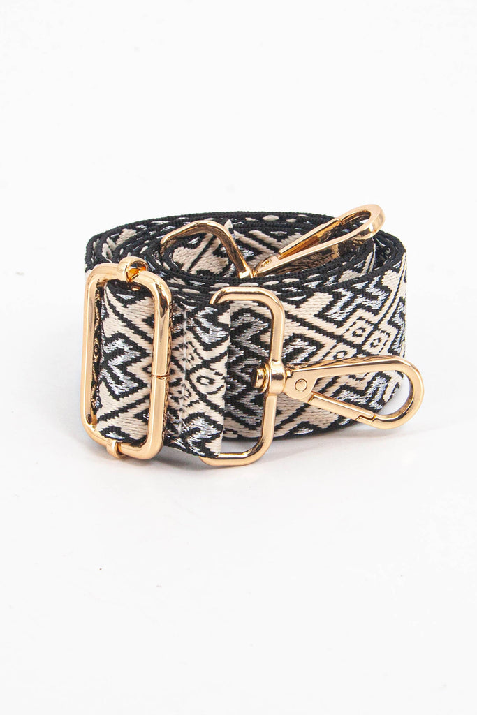 showing the bag strap coiled around itself, the navy blue and gold jacquard woven design is prominent , the gold hardware is shown in close up