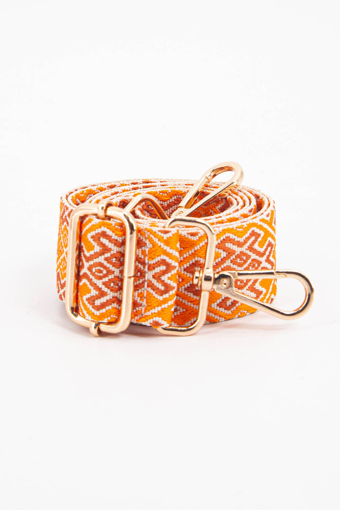 showing the bag strap coiled around itself, the ornate orange jacquard woven design is prominent , the gold hardware is shown in close up
