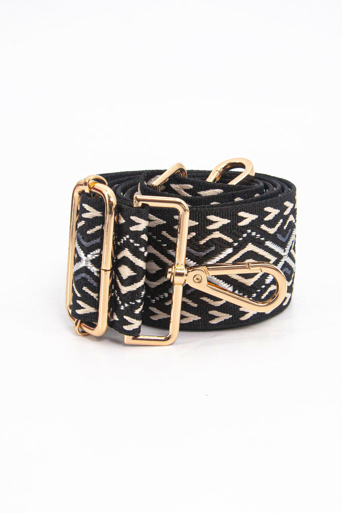 showing the bag strap coiled around itself, the ornate black and gold metallic woven design is prominent , the gold hardware is shown in close up