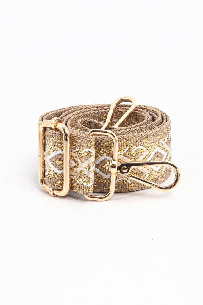 showing the bag strap coiled around itself, the ornate gold metallic woven design is prominent , the gold hardware is shown in close up