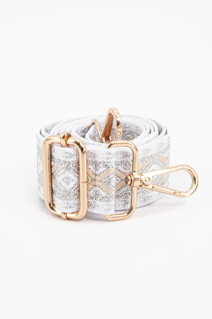showing the bag strap coiled around itself, the  silver and gold metallic woven design is prominent , the gold hardware is shown in close up