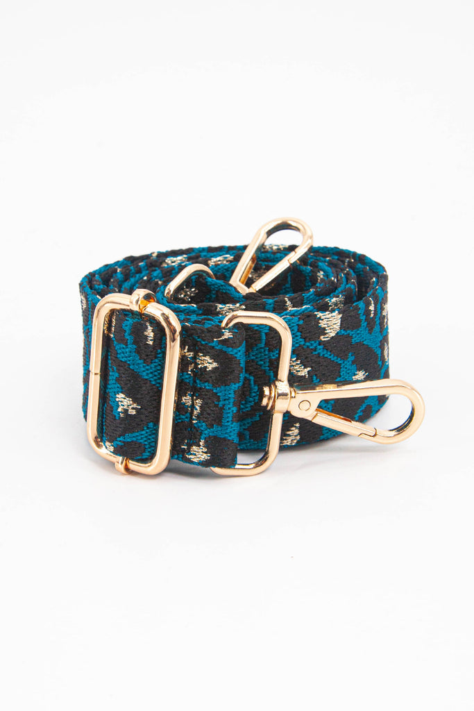 showing the bag strap coiled around itself, the blue and gold leopard print metallic woven design is prominent , the gold hardware is shown in close up