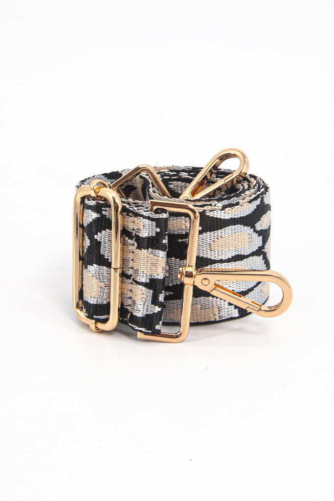 showing the bag strap coiled around itself, the black and gold metallic animal print woven design is prominent , the gold hardware is shown in close up