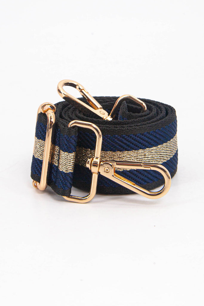 showing the bag strap coiled around itself, the navy blue and gold metallic stripe woven design is prominent , the gold hardware is shown in close up