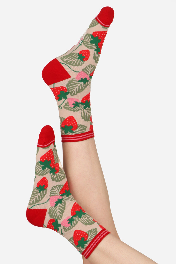 Ladies feet in the air wearing strawberry print socks. Contrasting red toe and heel can be seen