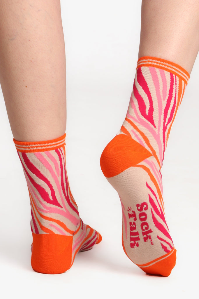 Model wearing bamboo zebra print socks. Posed with feet facing away from camera to show sole of sock which has sock talk logo