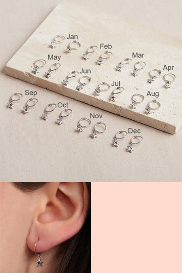 a selection of hoop earring with dangling star charms below the hoops, each month is represented by a different birthstone colour in the form of a small cz crystal in the middle of the star charm