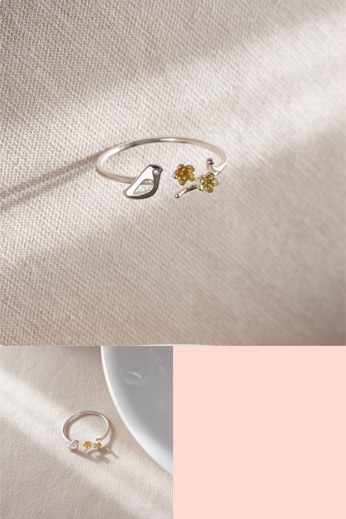 sterling silver open adjustable ring, designed to have a little bird on one side of the opening and a twig with flowers on the other, the flowers are gold plated sterling silver