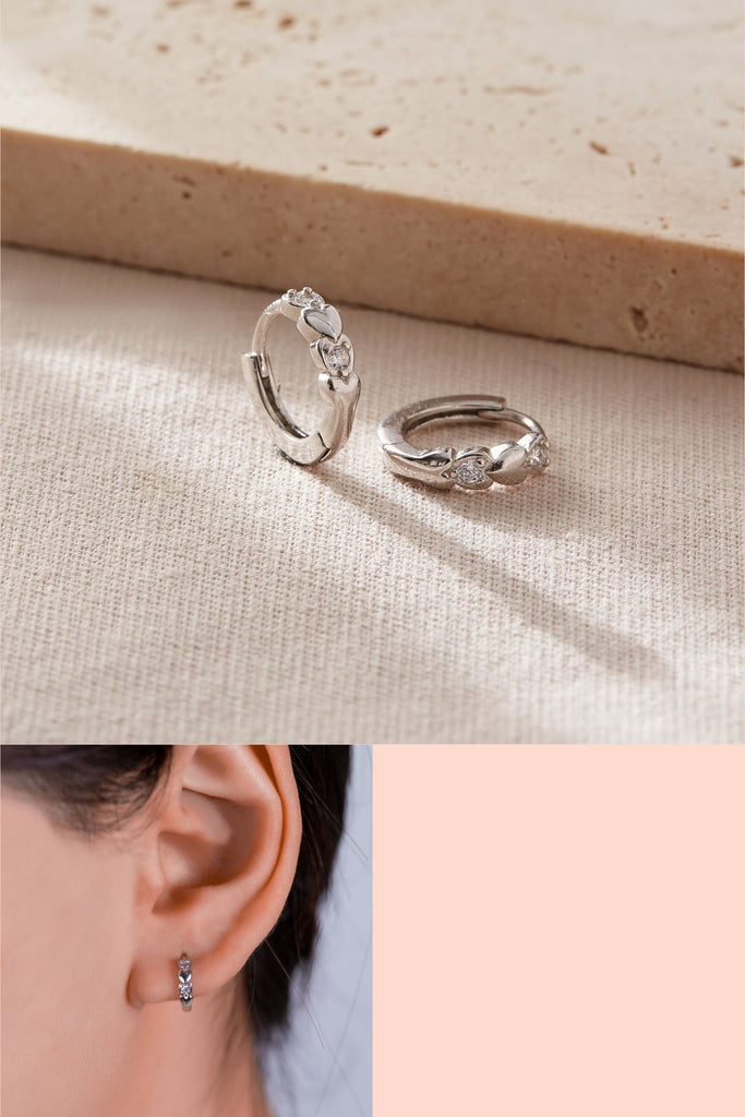 sterling silver huggie hoop earring embedded with two clear sparkly heart shaped cubic zirconia crystals and a solid silver heart shaped motif, the earrings are dainty and are latch back fastening