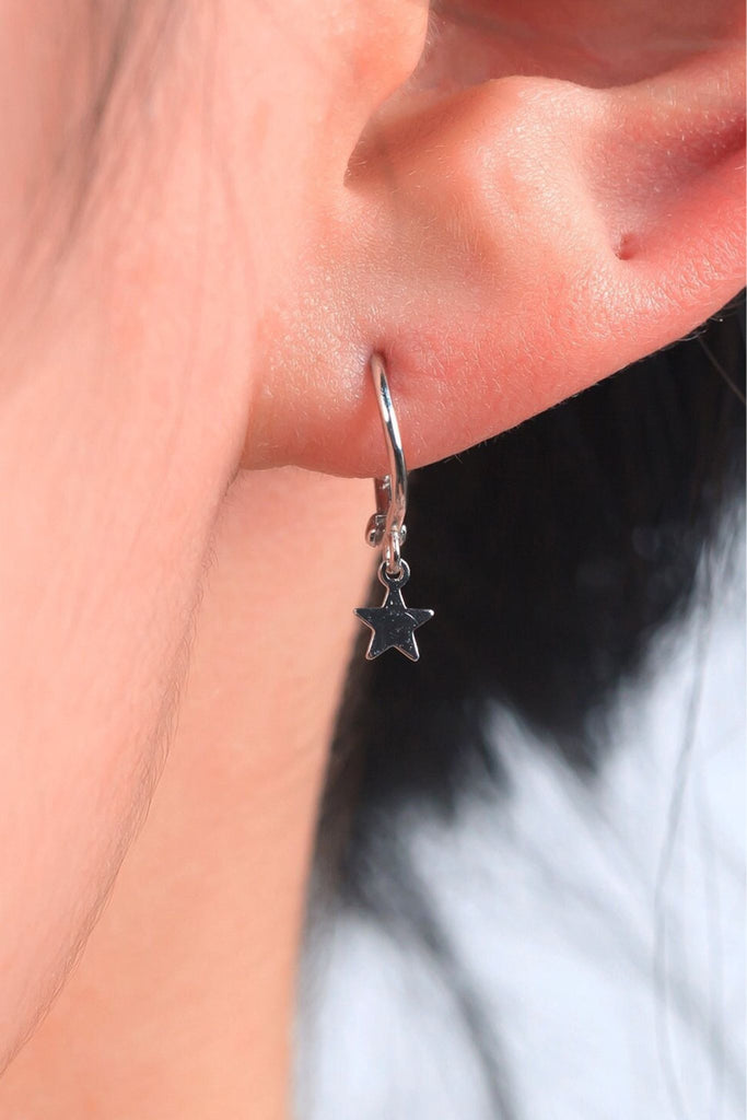 sterling silver hoop earring with a star charm, being worn on the earlobe