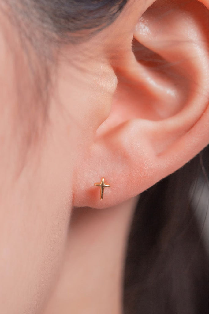 model showing the tiny cross stud being worn in the earlobe, showing the dainty size of the earrings