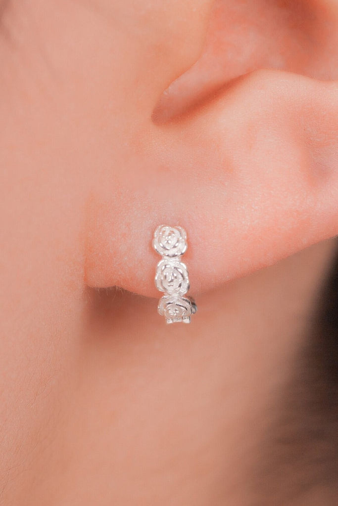 model wearing the silver rose hoop earring in the earlobe, showing the dainty size of the studs
