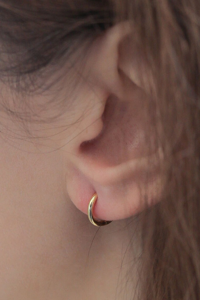 model wearing a gold huggie hoop earring in the earlobe