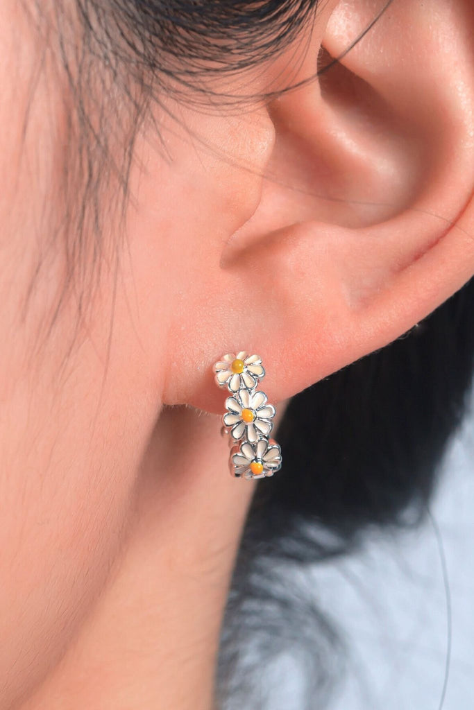 model wearing a white and yellow daisy chain huggie hoop earring in the earlobe