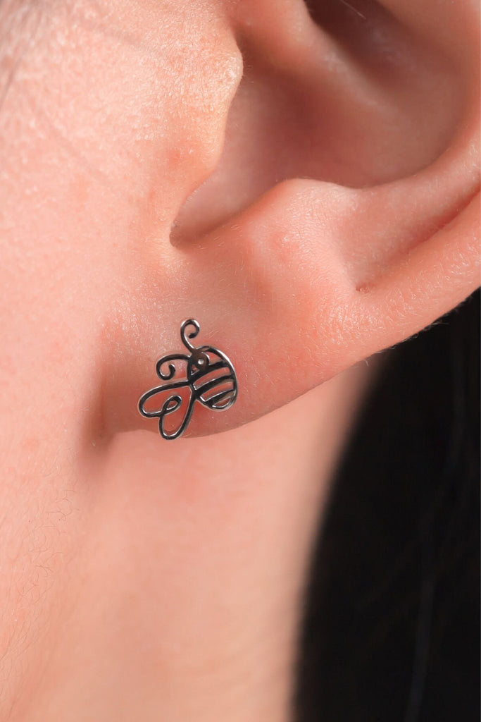 model wearing a dainty silver bee stud earring in the earlobe