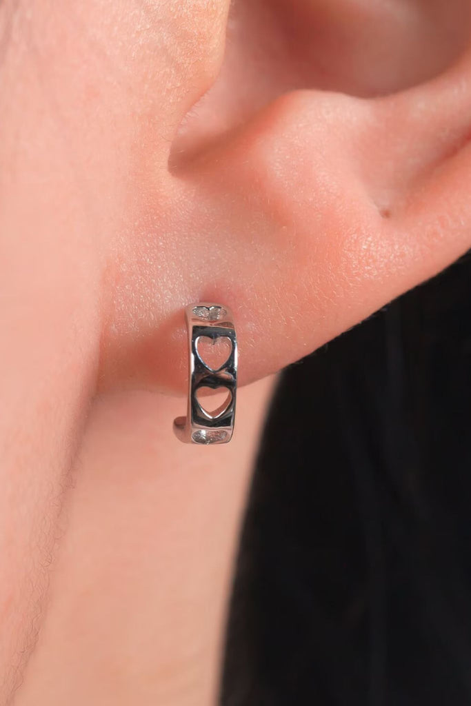 model wearing a half hoop earring with hollow heart shapes on the rim