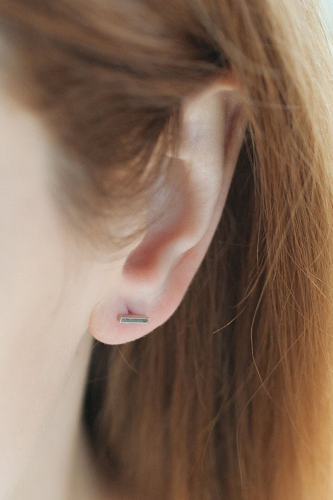 model wearing a silver bar stud on the earlobe, showing the dainty size of the sterling silver studs
