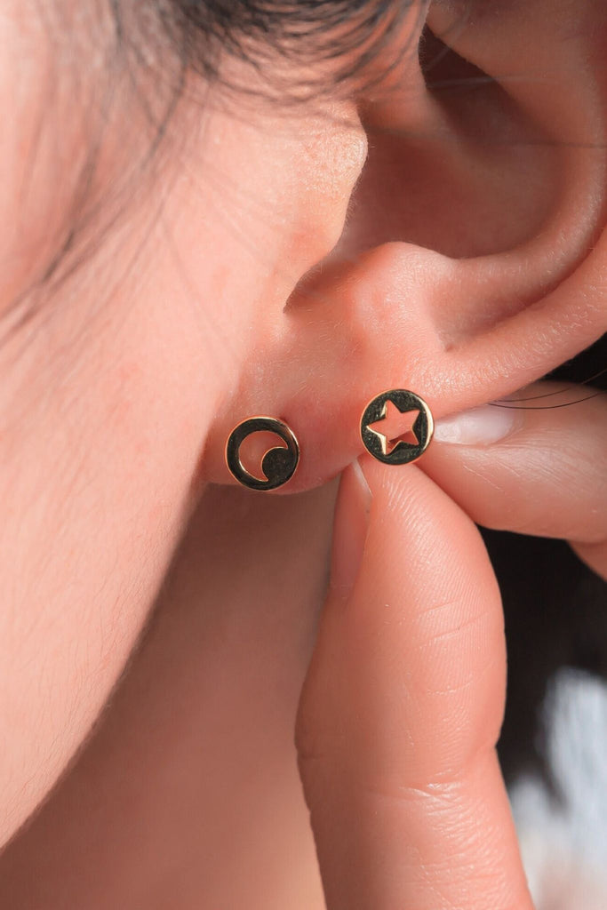 model wearing a gold moon stud on the earlob, showing the dainty size of the earrings. the model is also holding the hollow star earring beside the ear to show that these come as a pair