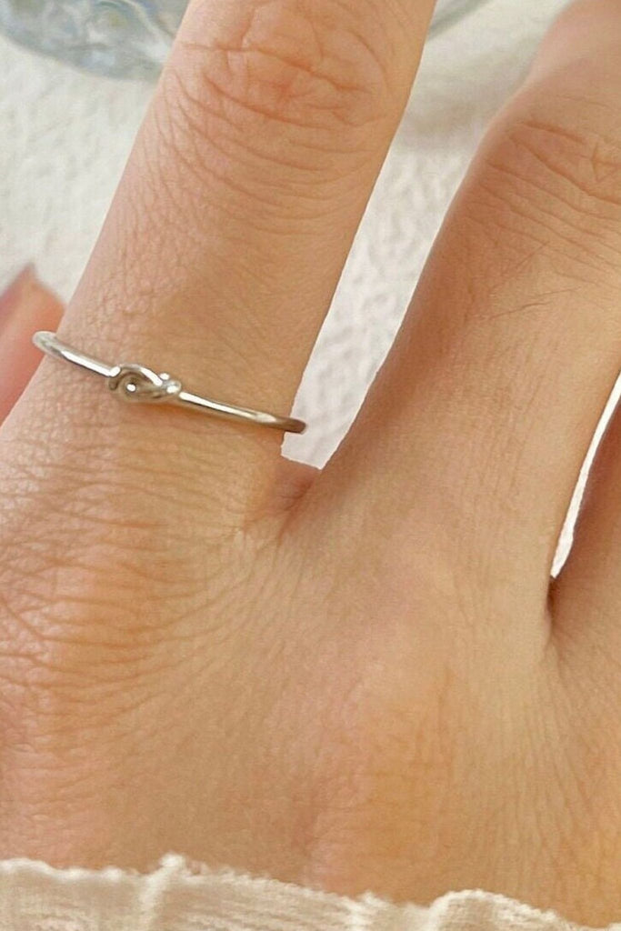model wearing this dainty ring on the finger, showing the thin band and the knot design