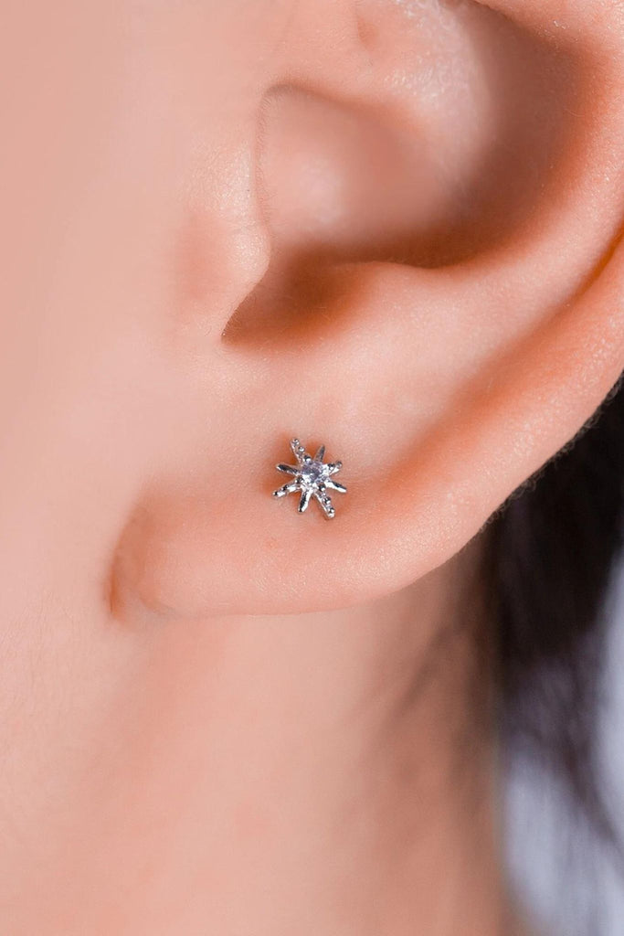 model wearing the silver starburst earring on the earlobe, showing the dainty size of the sparkly stud earrings