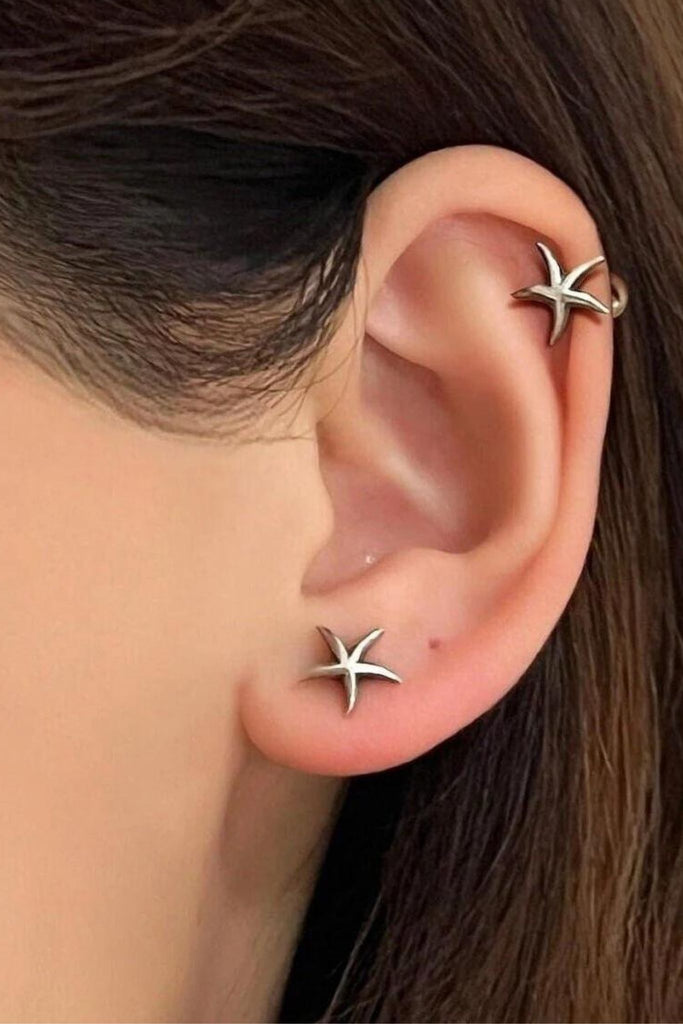 model wearing a pair of starfish stud earrings, showing that they can be worn as either a cartilage stud or in the earlobe 