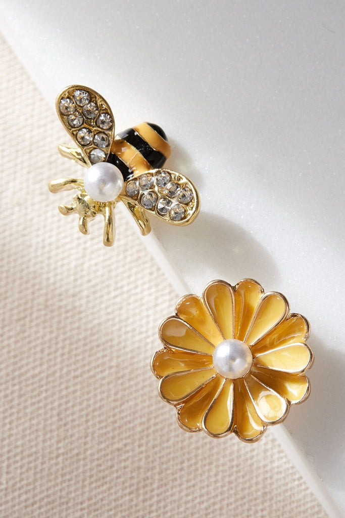 asymmetric stud earrings, one is a large yellow flower with a faux pearl in the middle, the other is a bumble bee with sparkly cz encrusted wings and a faux pearl accent