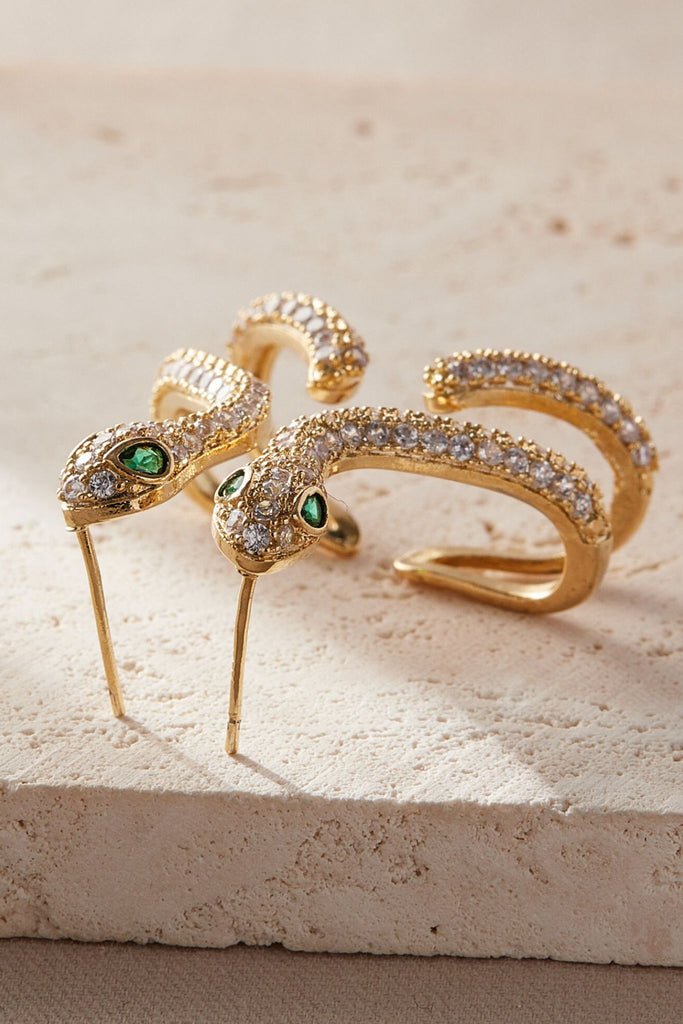 close up of the gold and white sparkly cz snake earrings from above, showing the intricate detail of the sparkly stones and green crystal eyes of the snake