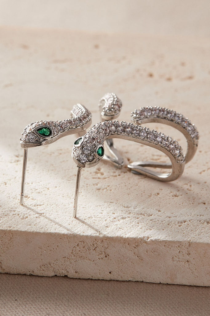 close up of the silver and white sparkly cz snake earrings from above, showing the intricate detail of the sparkly stones and green crystal eyes of the snake