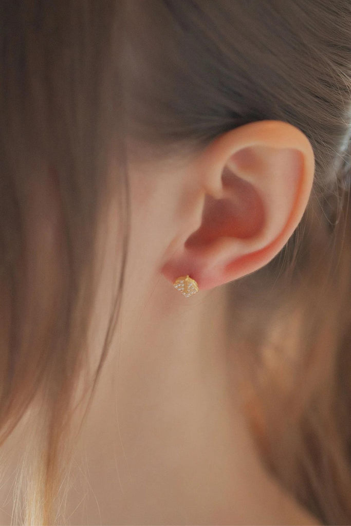 model wearing a gold coloured sparkly cz leaf stud earring on the earlobe, showing the dainty size of the earrings