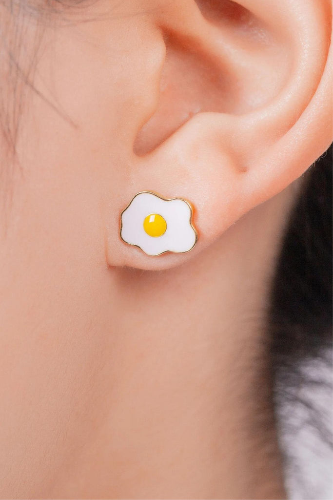 model wearing a fried egg stud earring in the earlobe, showing the size of the studs