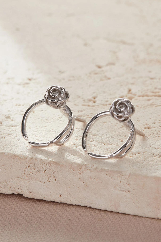 a pair of silver rose cuff earrings, showing the clip on fastening, the cuffs are placed over the rim of the ear and gently pressed into place