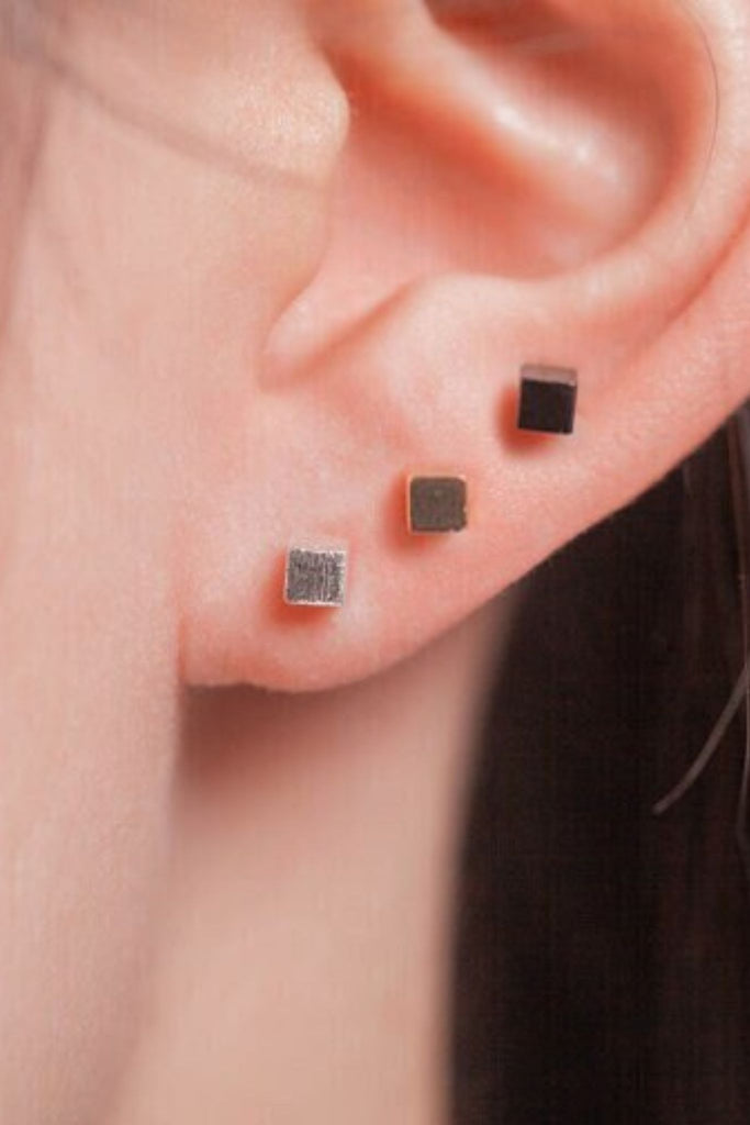 model wearing all three colours of square cube studs, silver, gold and black showing that the earrings can be stacked