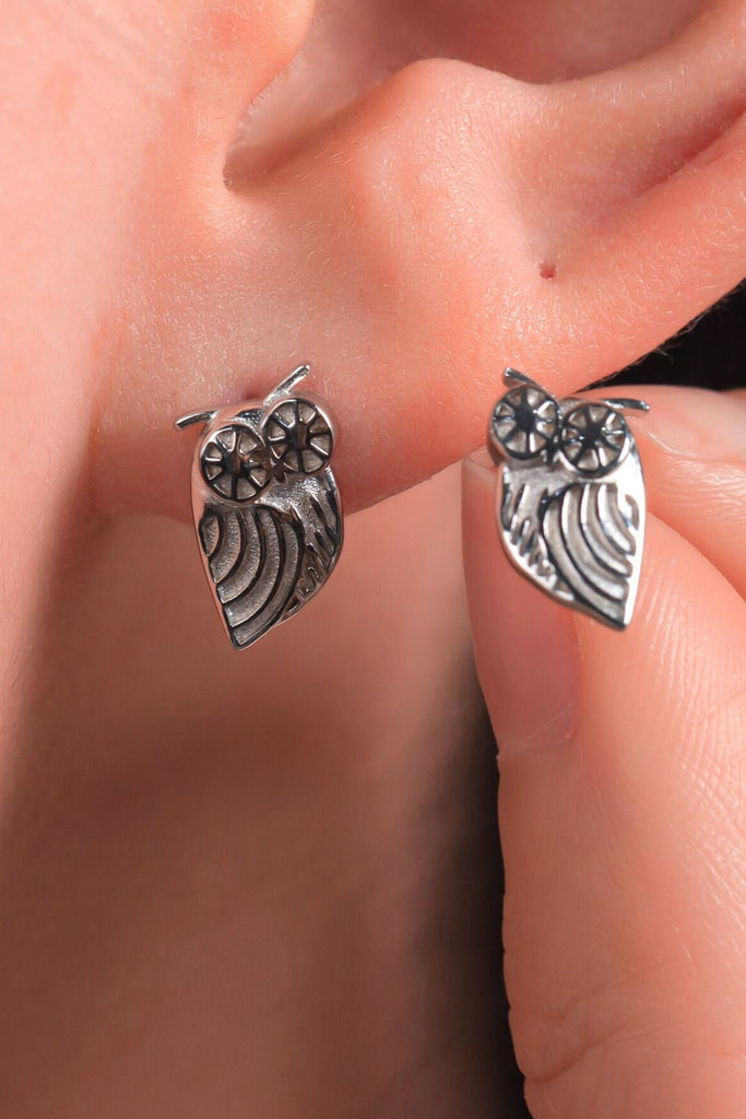 model wearing a silver owl stud earring, showing that the edge of the stud hangs just below the earlobe,