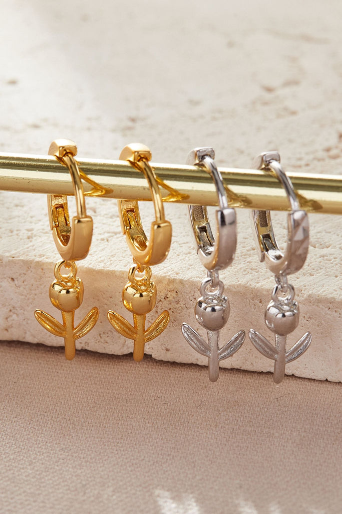 sterling silver and gold plated sterling silver dangle hoop earrings hanging on a rail, the hoops are huggie hoops with tulip flower charms attached to the bottom of them, the charms hang below the earlobe