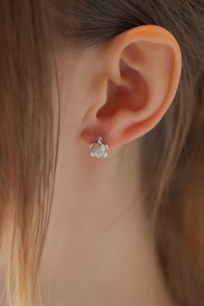 model wearing a sparkly turtle stud earring on the earlobe, showing the small size of the earrings