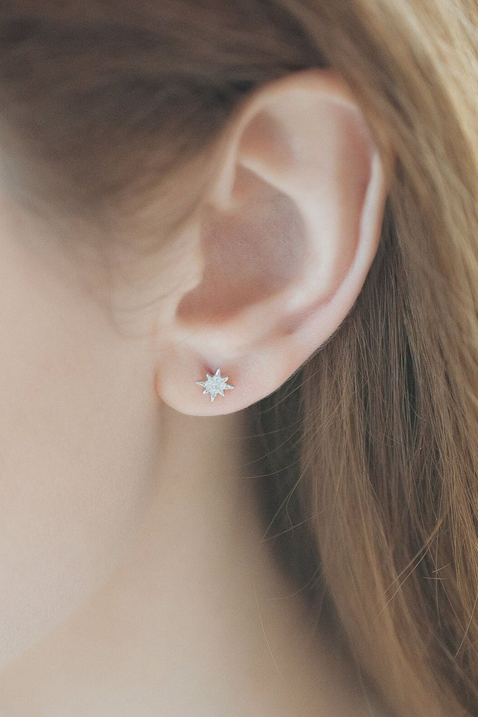 model wearing a silver sparkly eight sided starburst earring on the earlobe, showing the dainty size of the earrings