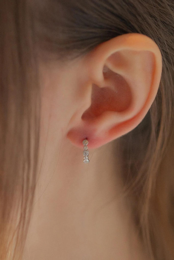 model wearing a silver beaded hoop earring on the earlobe, showing that they fit close to the ear