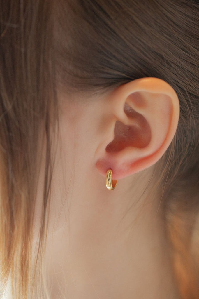 model wearing a gold coloured plain hoop earring on the earlobe, they are small but they do hang just below the earlobe
