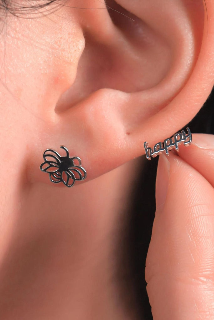 model wearing the silver bee stud and holding up the happy stud next to the earlobe showing the size of the earrings