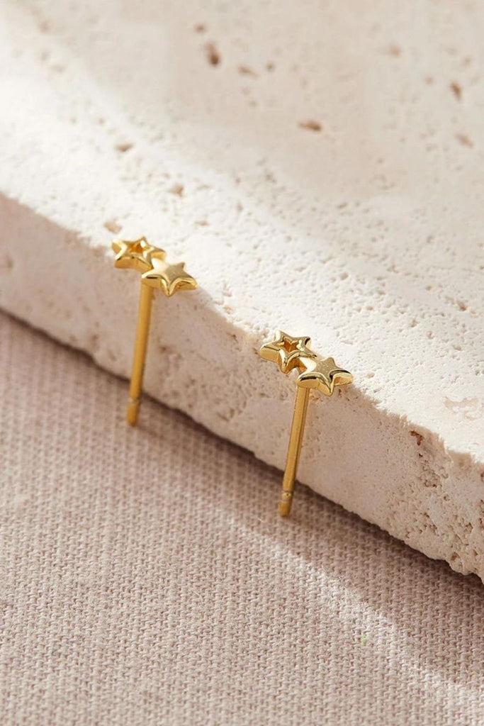 close up of the gold dual star earrings, showing one star as hollow and the other solid, both adjoined to each other 