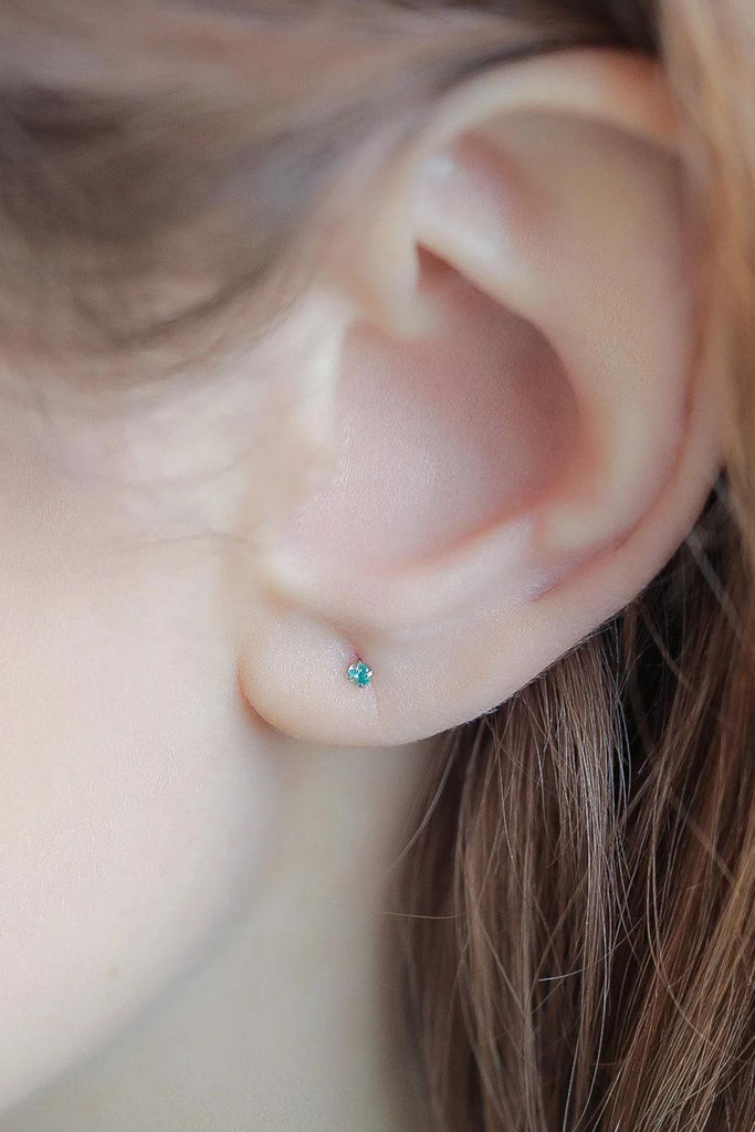 model wearing a blue dainty cz crystal stud earring in the earlobe showing the dainty size of the earrings