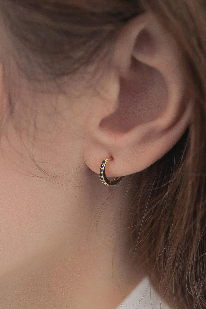 model wearing a gold and blue cz huggie hoop earring, showing the dainty size of the earring