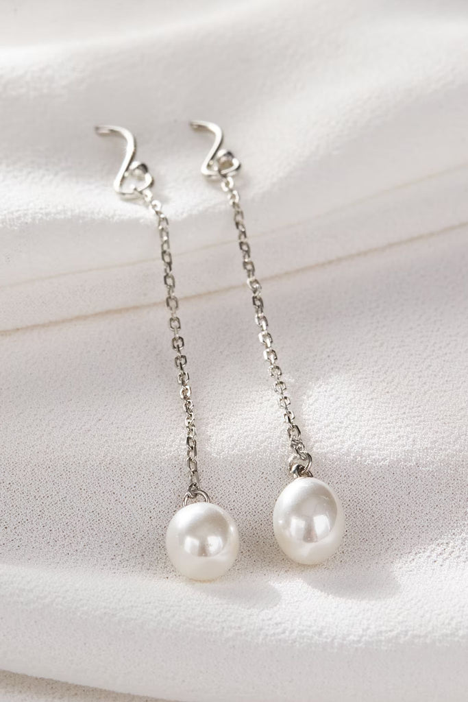 close up of the silver pearl dangle earrings, showing a close up of the white round pearls and silver hook backs