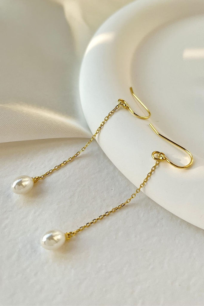 close up of the gold pearl dangle earrings, showing a close up of the white round pearls and gold hook backs