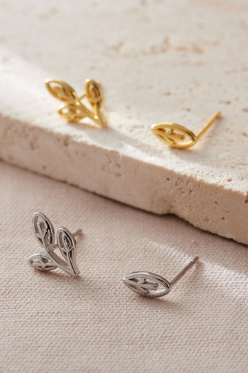 sterling silver and gold plated sterling silver mismatched leaf stud earrings, one is a single leaf, the other a small branch with three leaves. the leaves are oval and resemble olive tree leaves