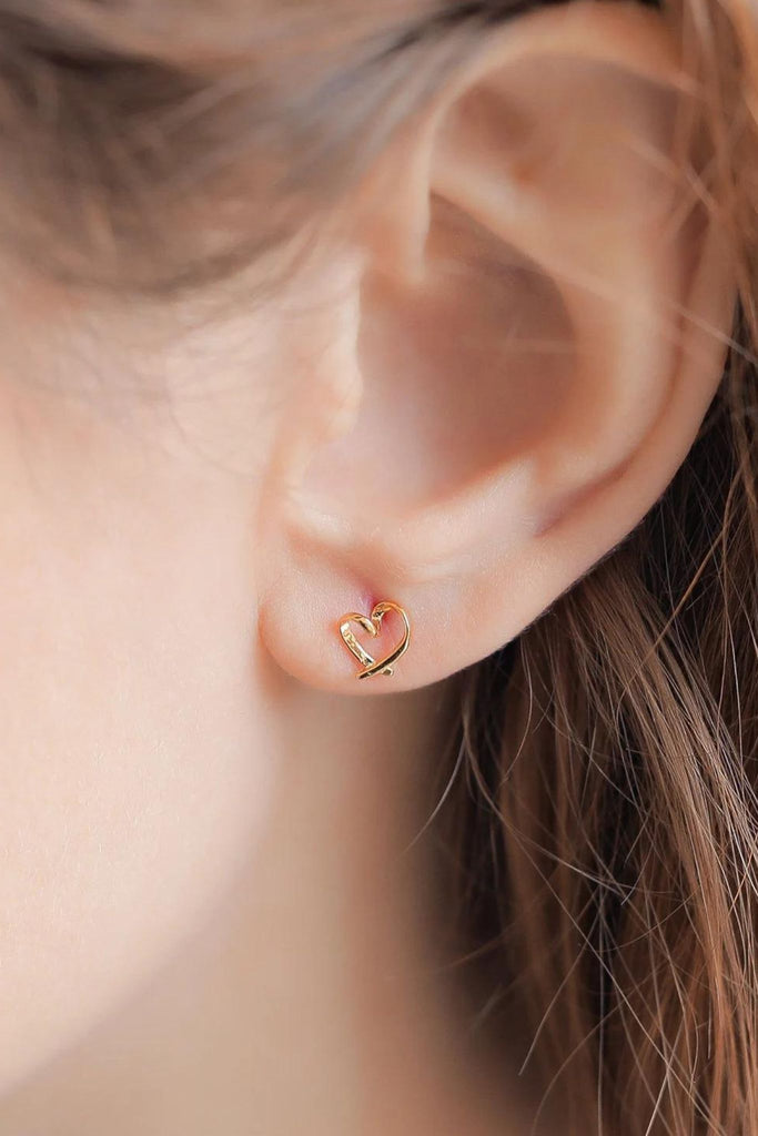 model wearing a gold abstract heart stud earring on the earlobe showing the dainty size of the earrings 