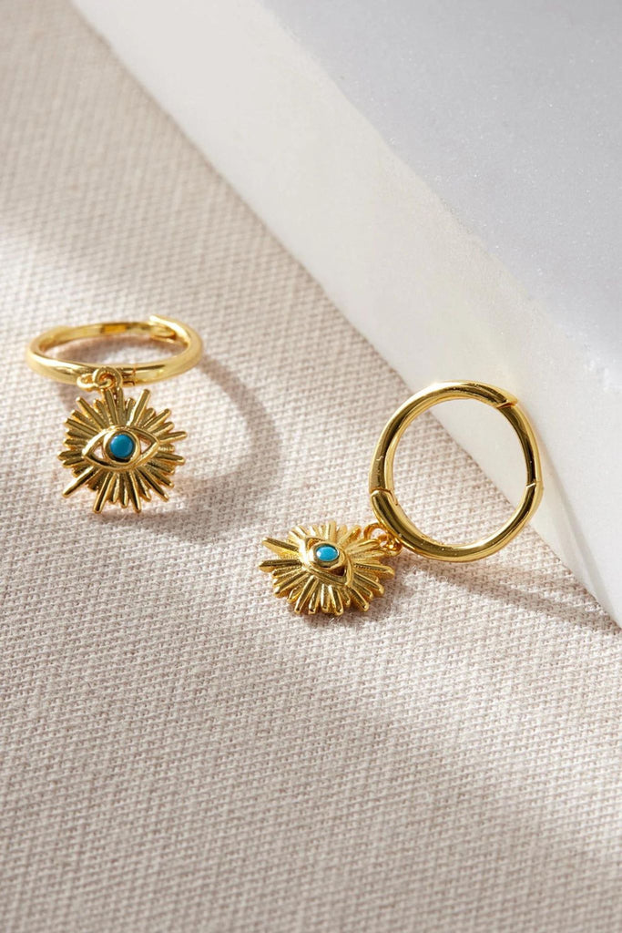 close up of the gold coloured evil eye charm earrings, showing a close up of the blue eye surrounded by sun rays